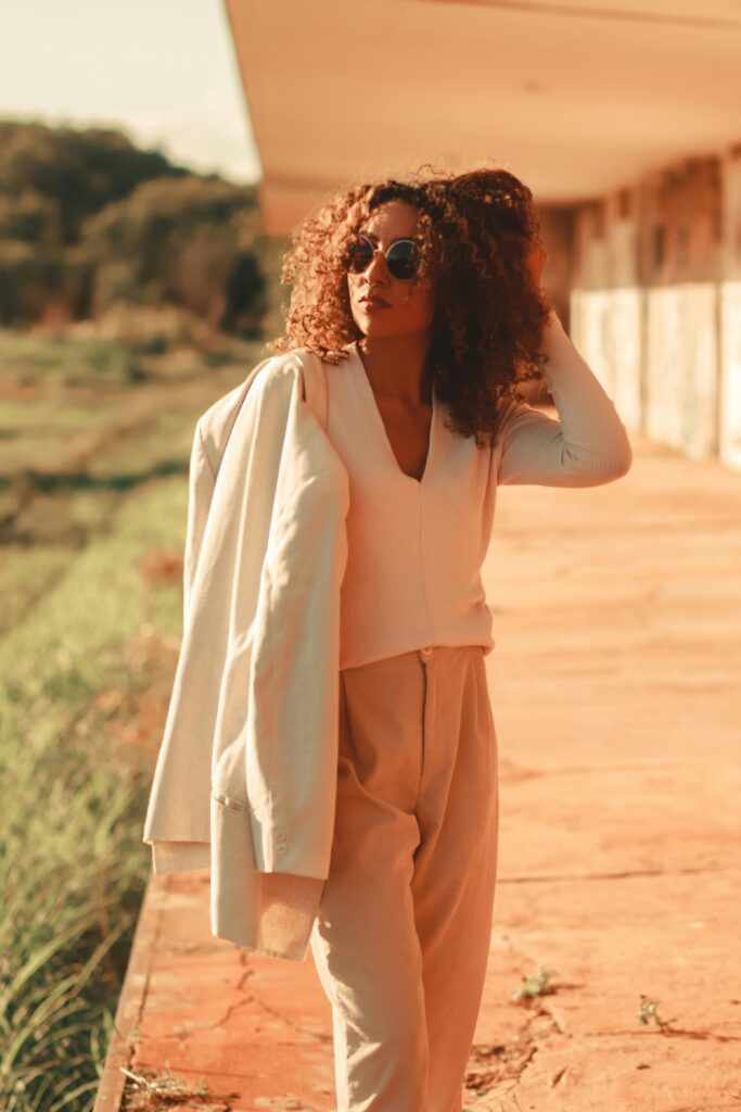 Trendy woman with curly hair poses in stylish outfit outdoors on a sunny day.